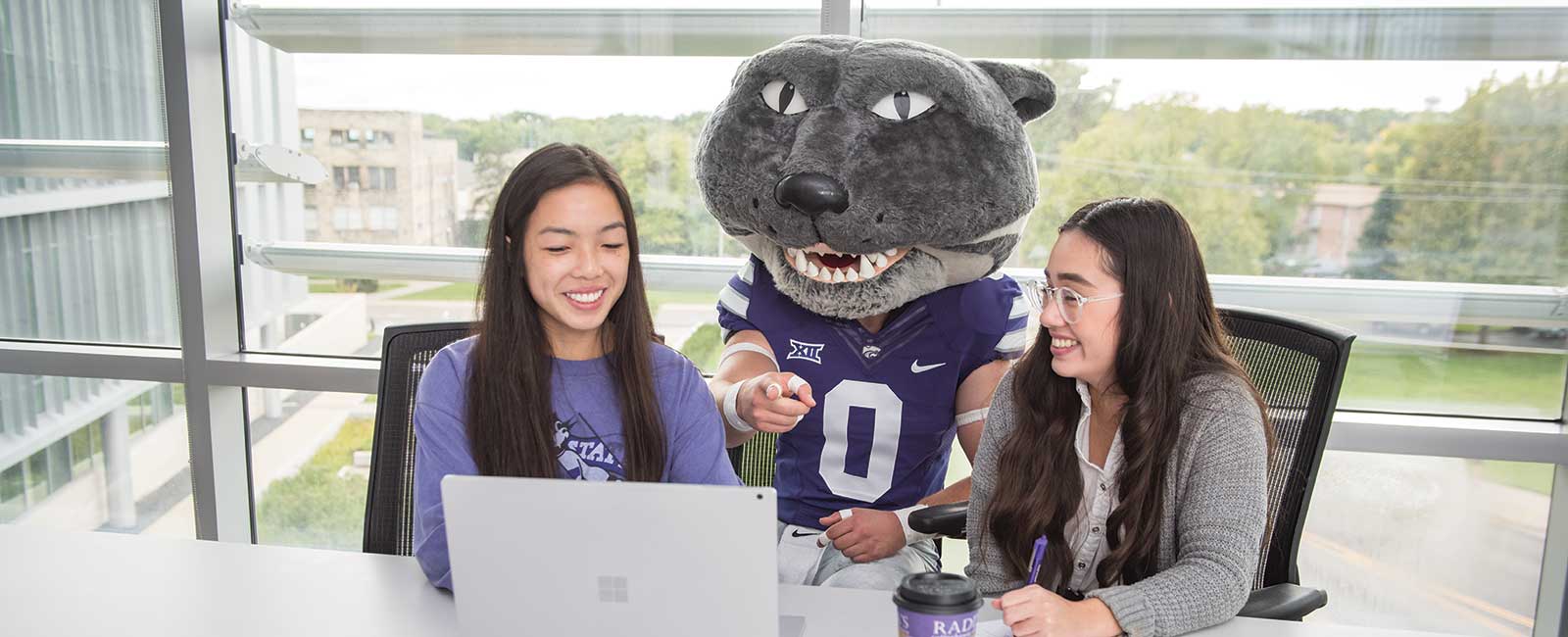 Two students work at a laptop with Willie the Wildcat