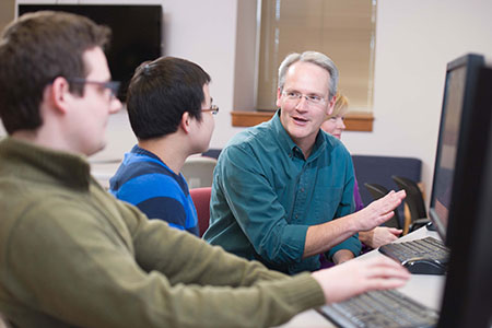 Faculty member talks to two students at computers.